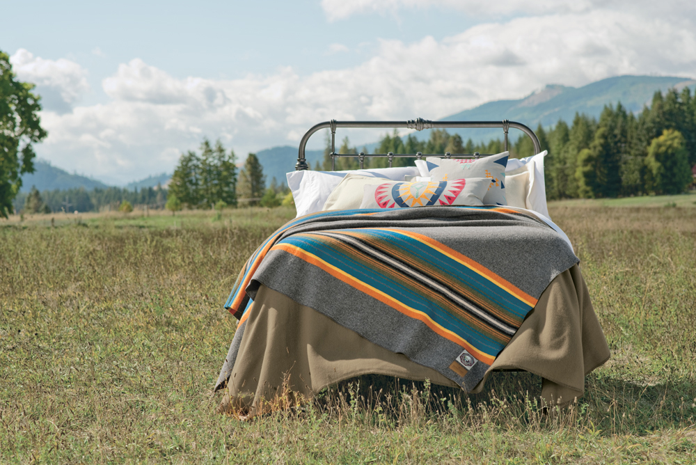 A bed made up with the Olympic national Park blanket by Pendleton sits in a mountain meadow.