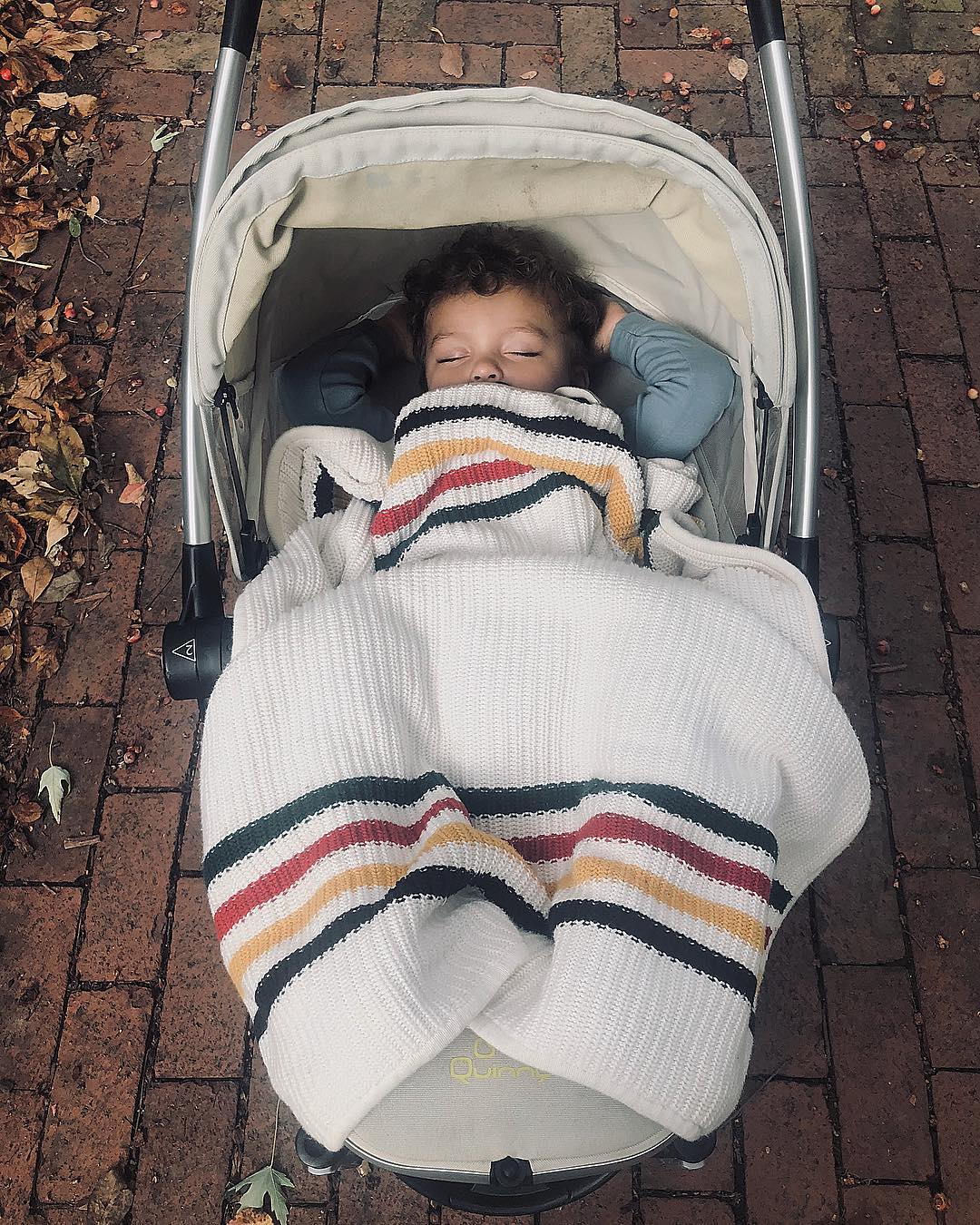 A toddler with adorable curly dark brown hair is asleep in a stroller, covered by a knitted Pendleton Glacier Park stroller blanket.