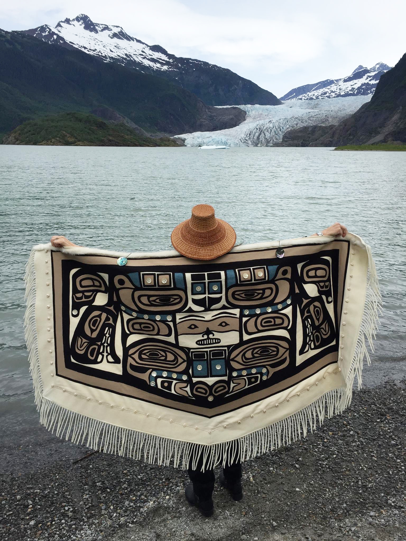 Linda Benson Kusumoto in her traditional Chilkat robe standing in front of the Mendenhall Glacier in Alaska.