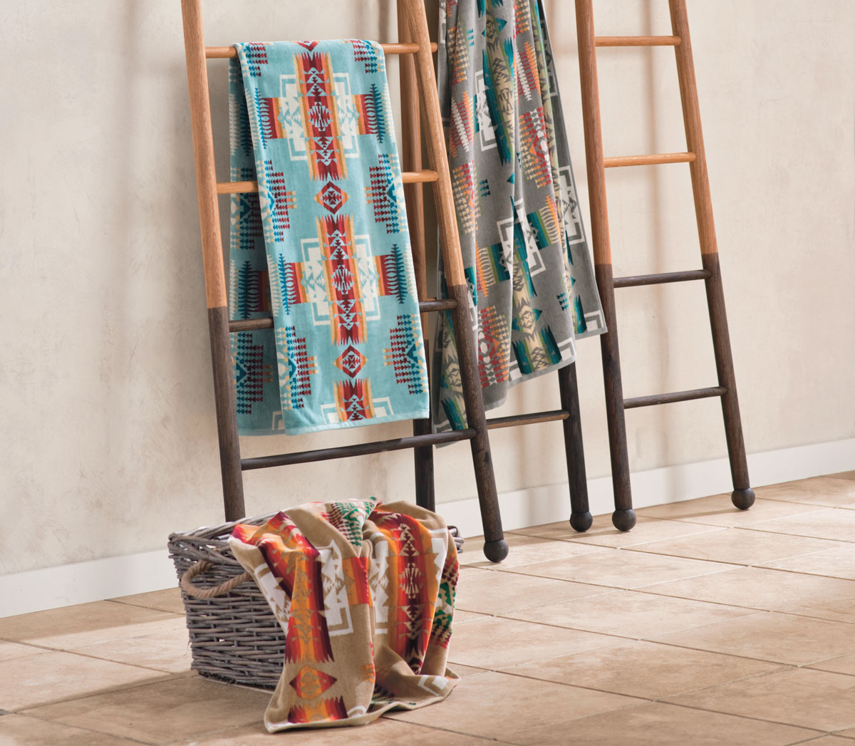 Colorful Pendleton beach and spa towels are draped on the rungs of three wooden ladders, and one is in a basket on the tile floor.