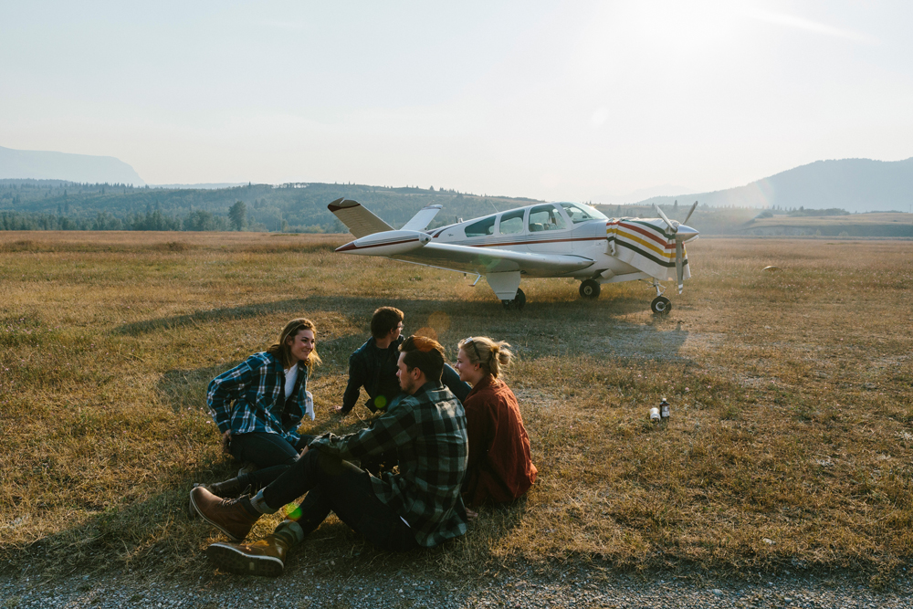 Irey_Four people sit on the ground in front of a small airplane. They are wearing Pendleton wool shirts