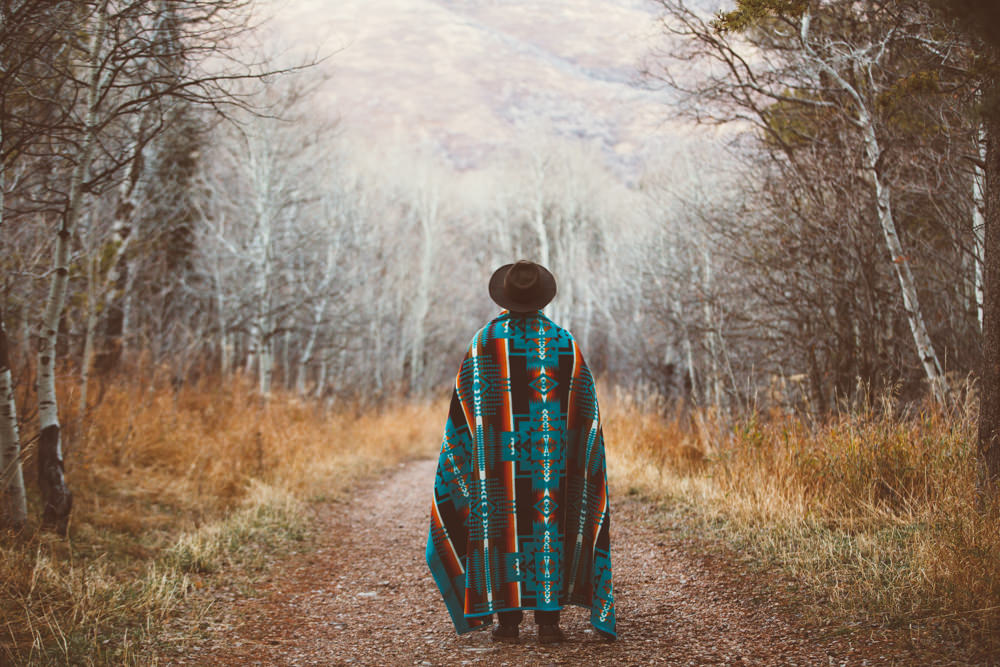 A man wrapped in a blanket stands on a mountain road.