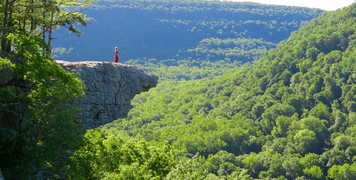 A woman stands on a rocky outcropping, taking in a view of the Ozark Mountains. Photo by Greg Hatten