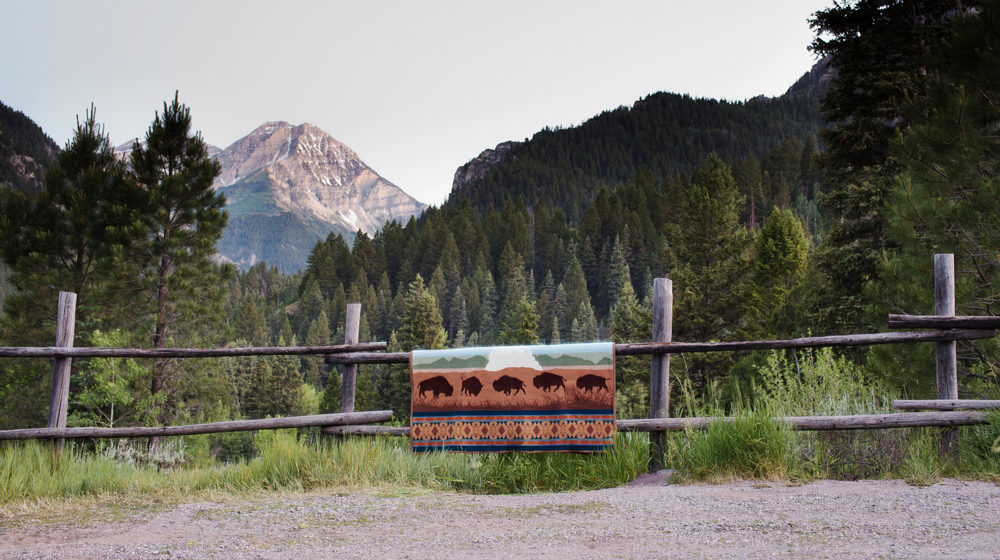 Brandon Burk the Yellowstone Centennial blanket draped over a rail vence, mountain in the background