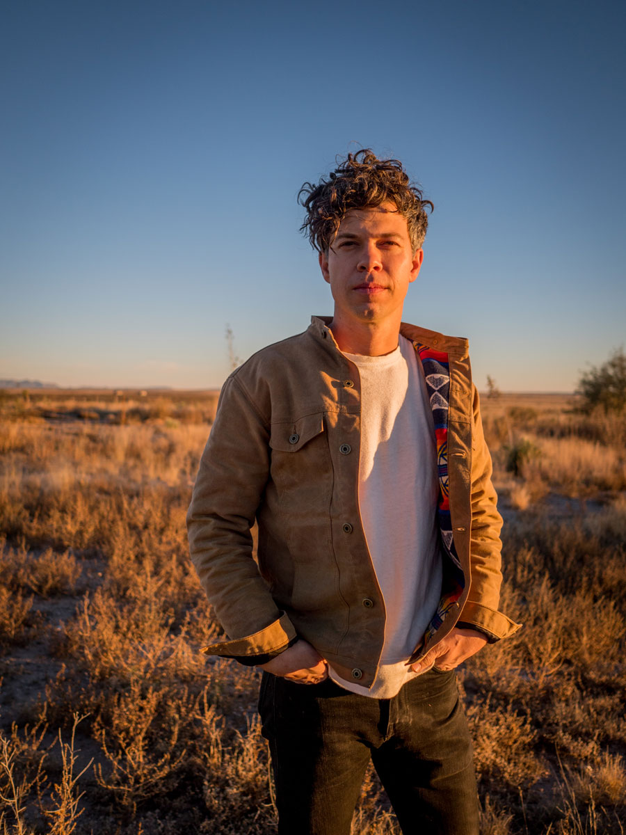 Aman stands in a field of dry grass, wearing a Ginew x Pendleton work jacket.