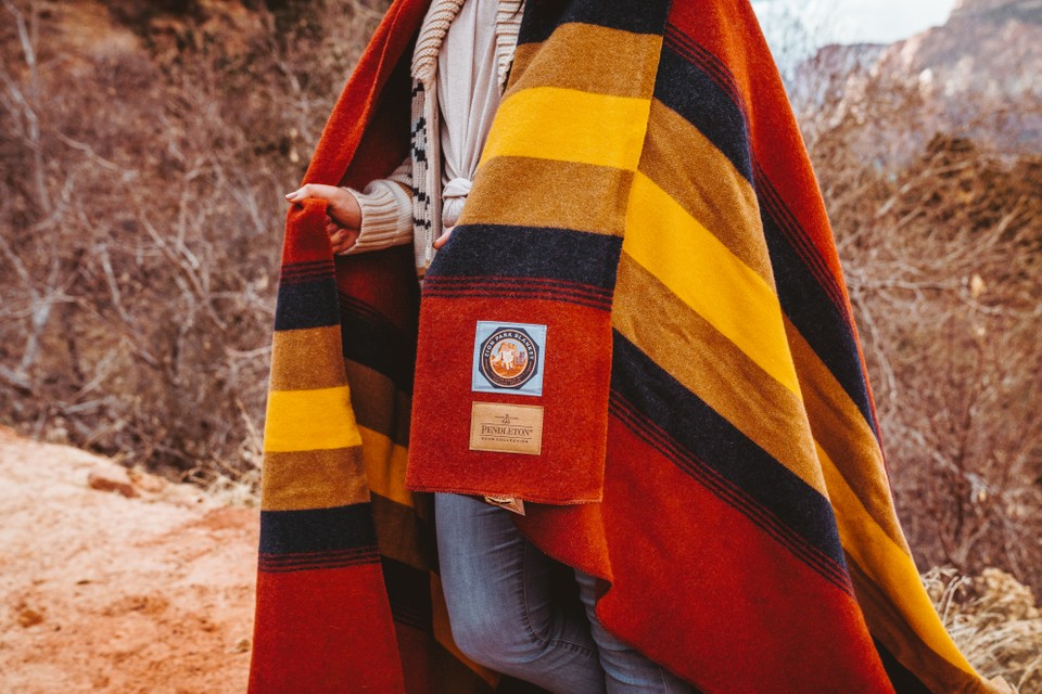 A girl stands in Zion National Park with the Zion blanket around her shoulders.