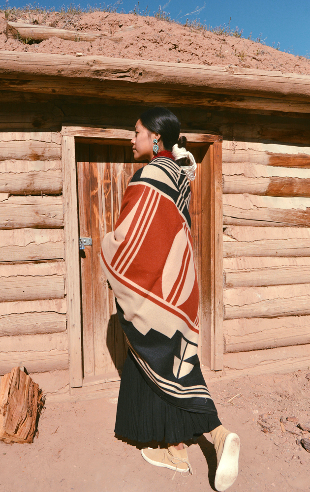 Shondina Lee Yikasbaa poses in traditional Dine clothing, family jewelry, and the Gift of the Earth blanket. 