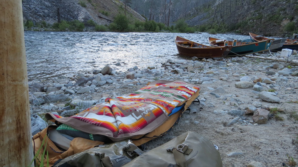 Greg Hatten makes camp on the banks of the Middle FOrk of the Salmon RIver, with his cot, Pendleton blanket, and boats in the distance.n Photo by Greg Hatten