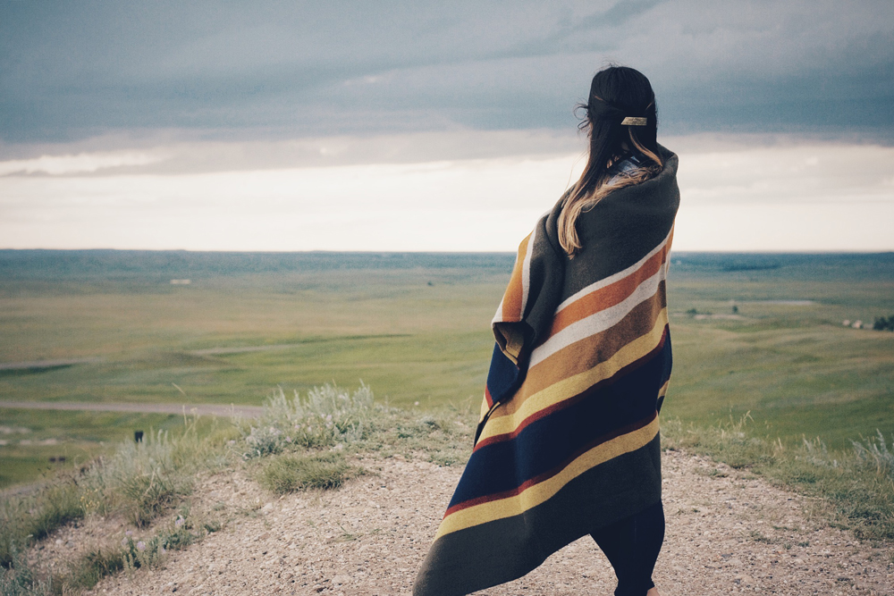 A woman wrapped in a Pendleton blanket looks out on the prairie