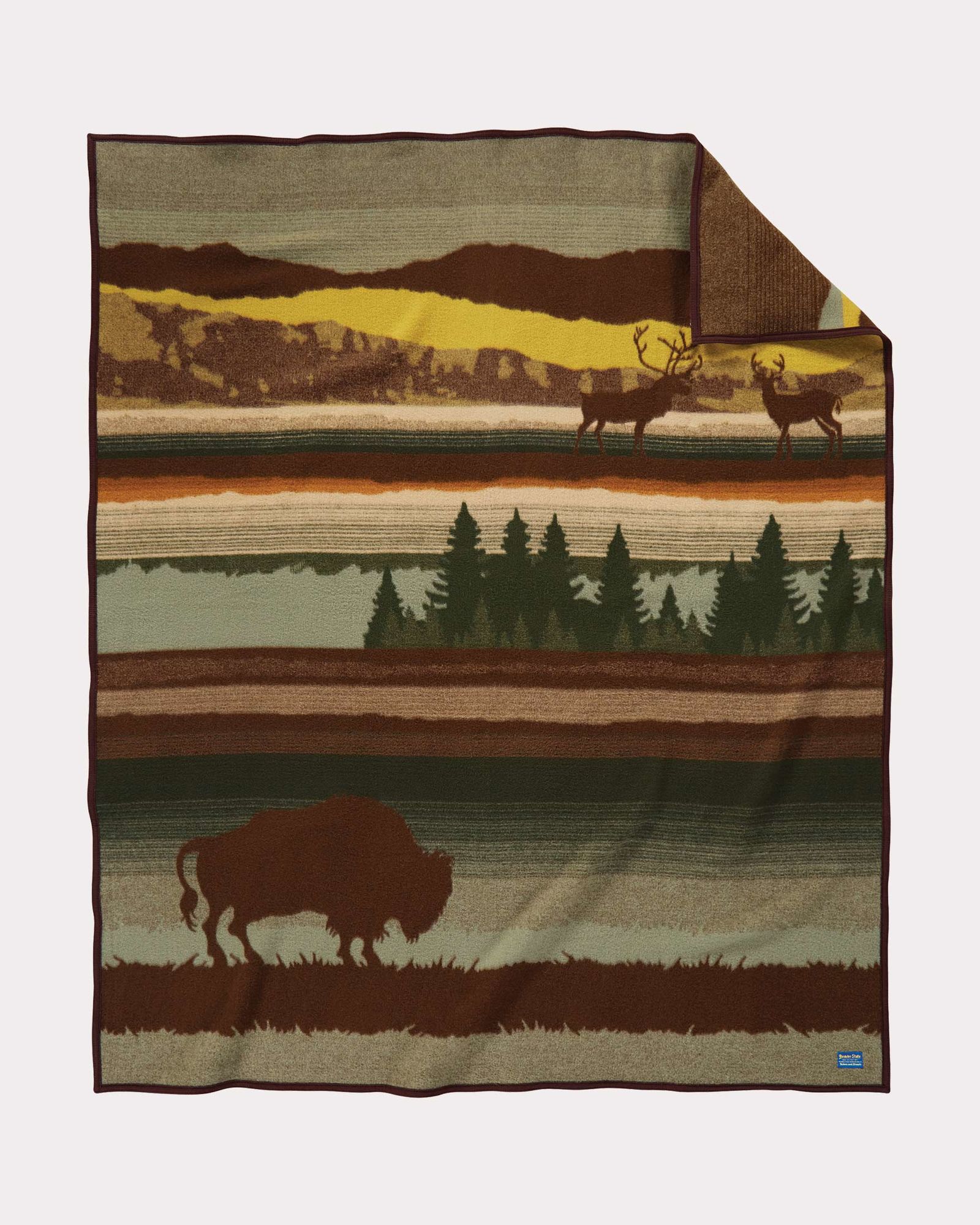 The Buffalo Wilderness blanket by Pendleton shows a buffalo (or bison) in silhouette against a landscapr of green, brown and gold. At the top of the blanket, two elk are shown in silhouette.