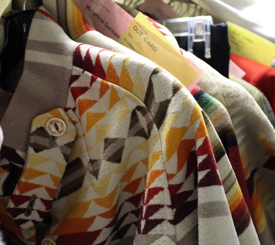 A group of vintage Pendleton blanket coats hanging together in the Pendleton archives. Yellow and pink pieces of paper calle d"out cards" are interspersed, showing where garments have been checked out of the archives for design inspiration. 