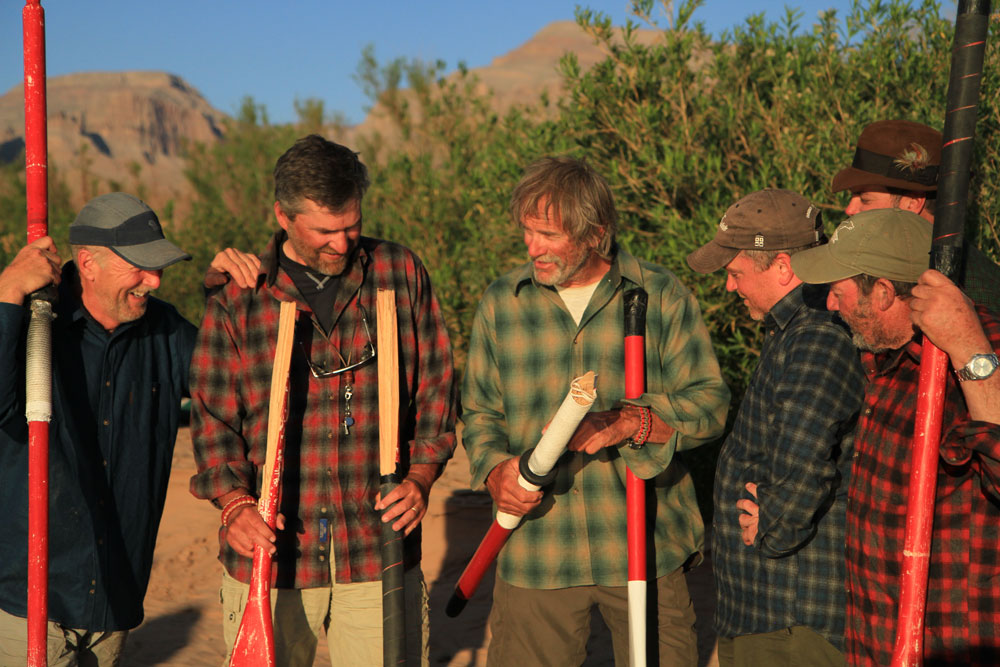 A rough and ready group of "River Rats," five men wearing Pendleton shirts, holding broken oars from their river running adventures.