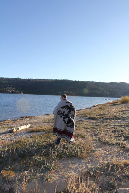 Man stands on shore of lake wrapped in USMC blanket by Pendleton.