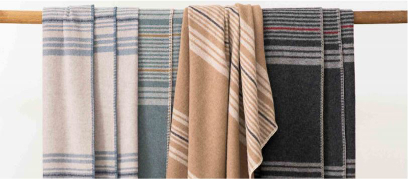 Four Pendleton Eco-Wise Wool striped throws draped across a wooden dowel. 