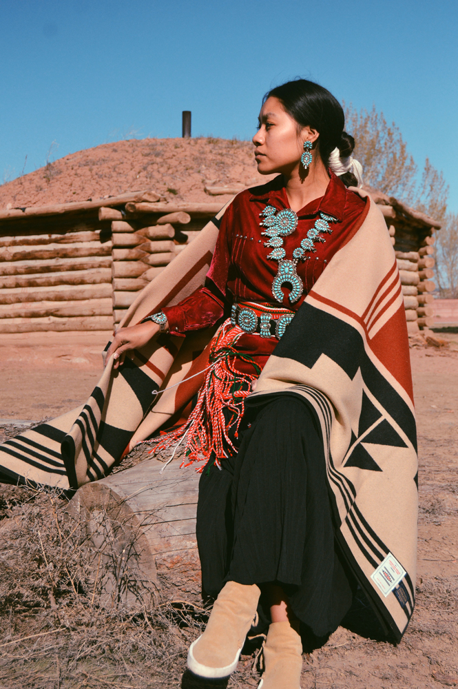 Shondina Lee Yikasbaa poses in traditional Dine clothing, family jewelry, and the Gift of the Earth blanket. 