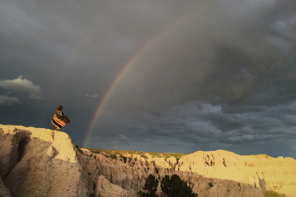 a woman on a bluff, a rainbow in the sky